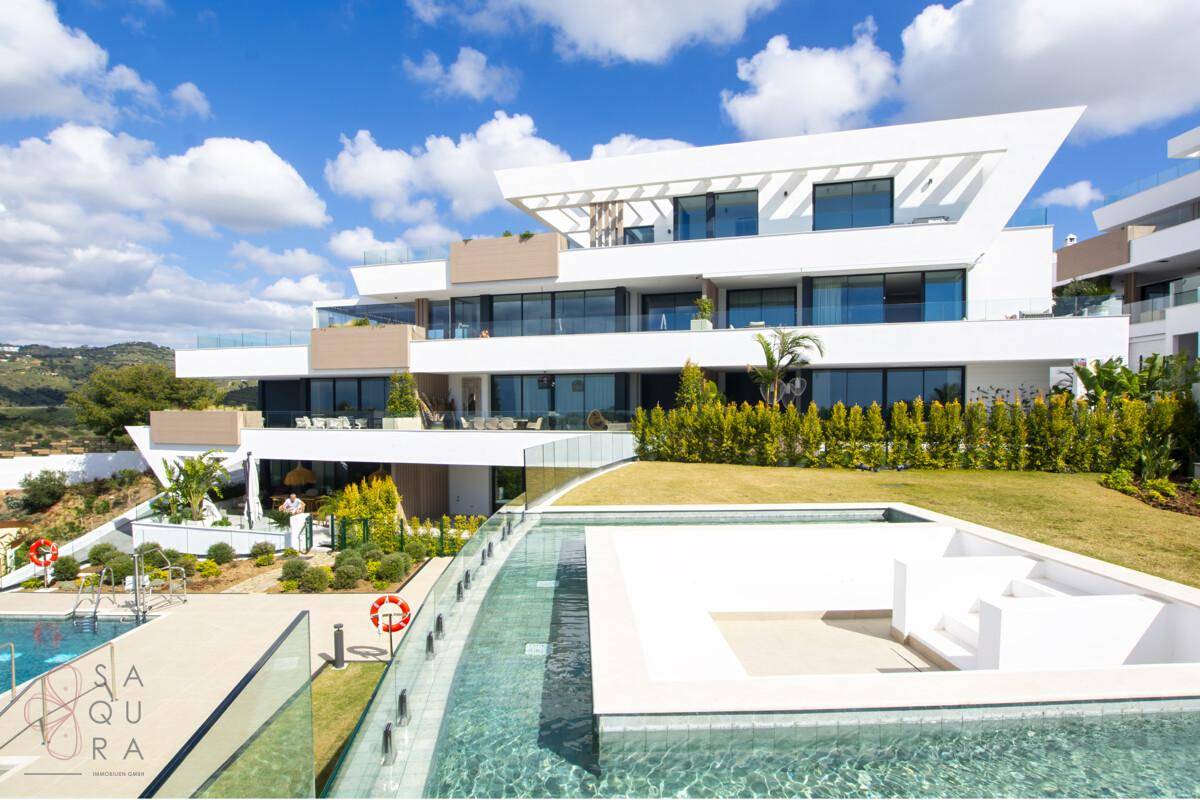 Weitläufige Außenanlage eines modernen Wohnkomplexes mit Pool, Grünflächen und Bergblick.