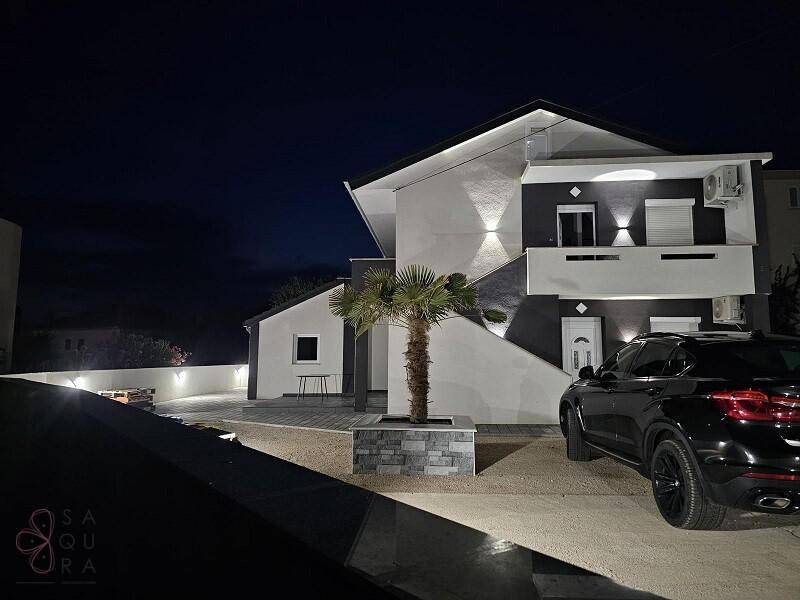 Ansicht des modernen Hauses bei Nacht mit akzentuierter Beleuchtung und einer Palme im Vordergrund.