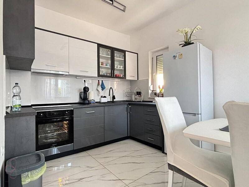 Moderne Küche mit weißen und grauen Schränken, integriertem Backofen und einem Fenster für natürliches Licht.