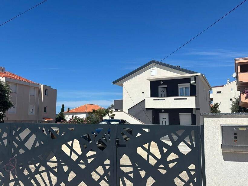 Modernes Haus hinter einem dekorativen Metalltor, mit weißer und schwarzer Fassade und blauem Himmel.