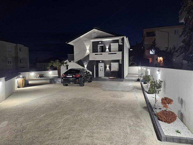 Beleuchtetes modernes Haus bei Nacht mit stilvoller Außenbeleuchtung und gepflegtem Vorplatz.