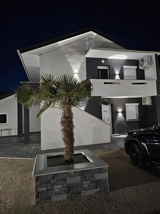 Beleuchtetes modernes Haus bei Nacht mit einer Palme im Vorgarten und stilvoller Fassadenbeleuchtung.