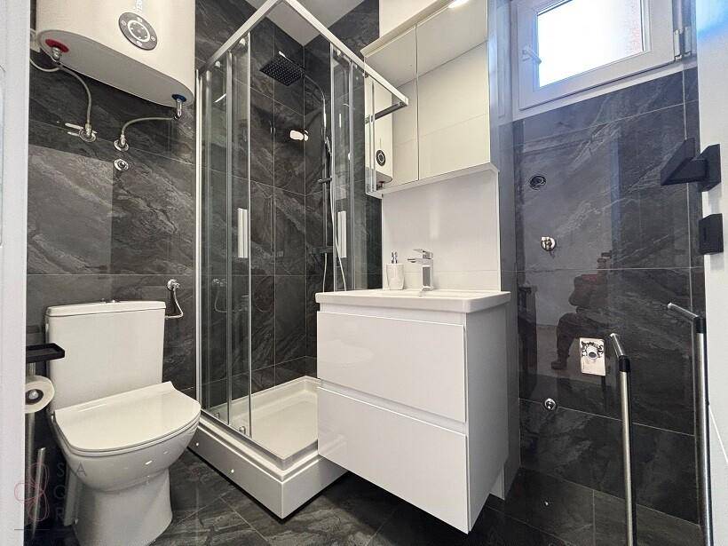 Modernes Badezimmer mit Duschkabine, WC, Waschtisch und Fenster, ausgestattet mit dunklen Fliesen.