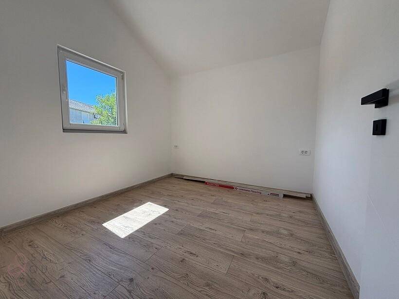 Heller, leerer Raum mit Holzboden und einem Fenster, das viel Tageslicht hereinlässt.