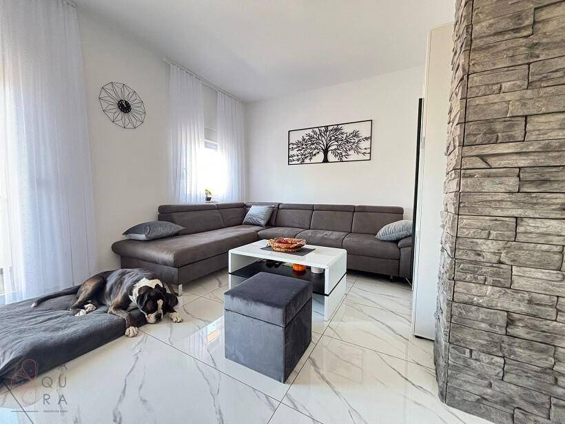 Gemütliches Wohnzimmer mit großem Ecksofa, modernen Fliesen und einem dekorativen Wandelement.