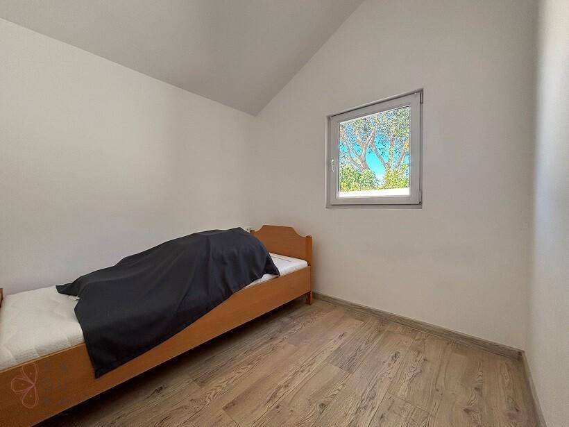 Gemütliches Schlafzimmer mit Einzelbett, Holzboden und Fenster mit Blick ins Grüne.