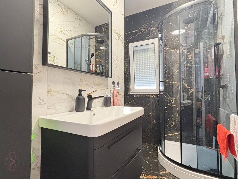 Modernes Badezimmer mit dunklen Marmorfliesen, elegantem Waschbecken und einer runden Duschkabine.