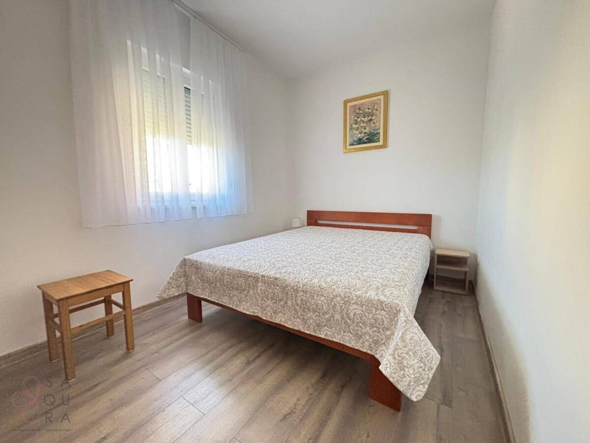 Helles Schlafzimmer mit Einzelbett, Holzoptik-Boden und einem Fenster mit weißem Vorhang.