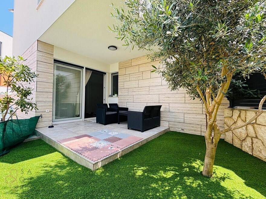 Gemütliche Terrasse mit Sitzgelegenheiten und Zugang zum kleinen Gartenbereich mit Olivenbaum.