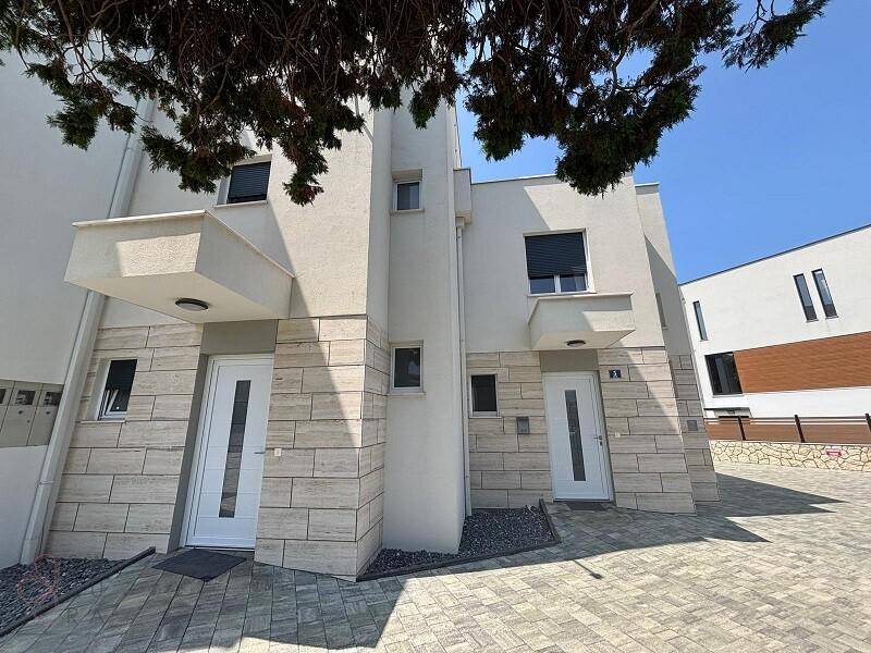 Moderne Gebäudefassade mit klaren Linien und gepflasterter Zufahrt, Neubau.