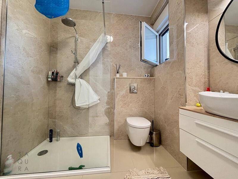 Modernes Badezimmer mit beigefarbenen Fliesen, ebenerdiger Dusche und wandhängendem WC.