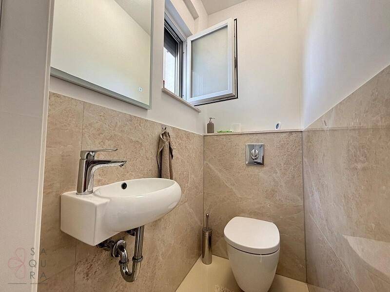 Kleines Gäste-WC mit wandhängendem Waschbecken und Toilette, hell gefliest.