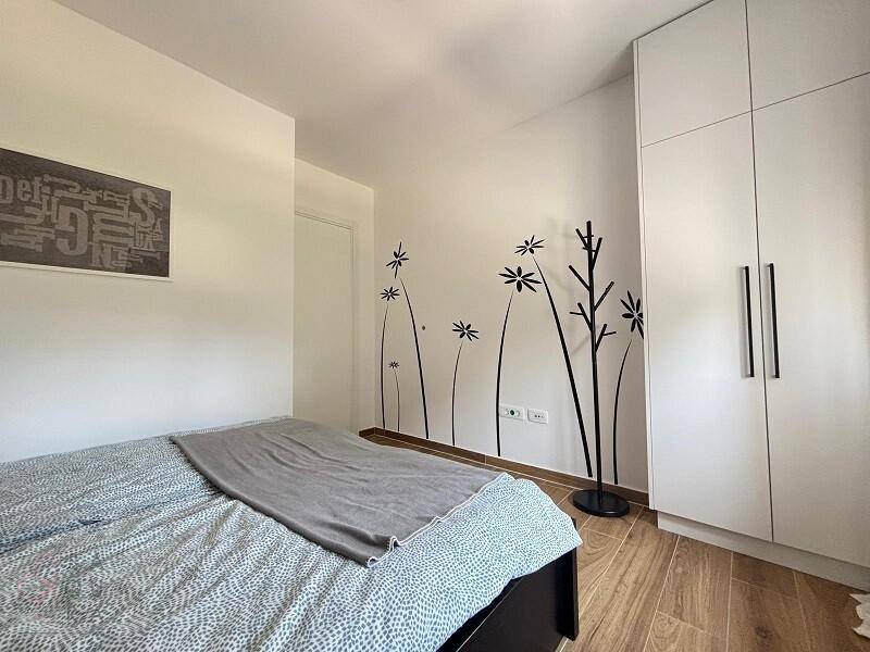 Helles Schlafzimmer mit Doppelbett, weißem Kleiderschrank und floralen Wanddekorationen.
