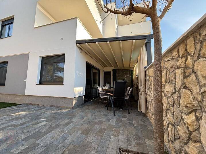 Überdachte Terrasse mit Steinboden und Esstisch, umgeben von einer Natursteinmauer.