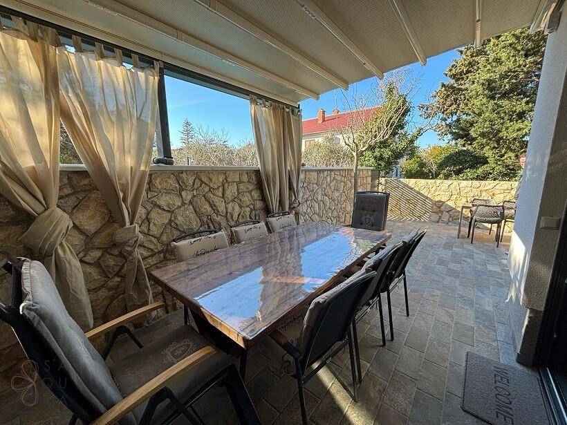 Gemütlicher Essbereich auf der überdachten Terrasse mit großem Tisch und Vorhängen.