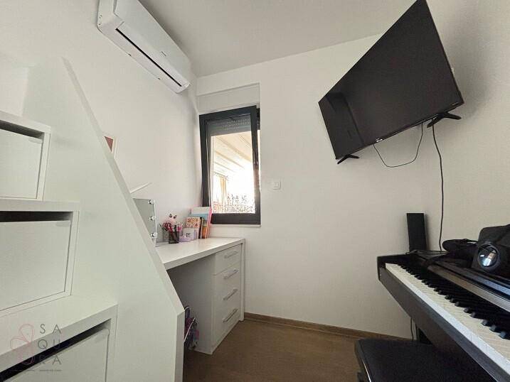 Helles Zimmer mit Schreibtisch, Klavier und Wandfernseher, ideal für Kinder oder Büro.