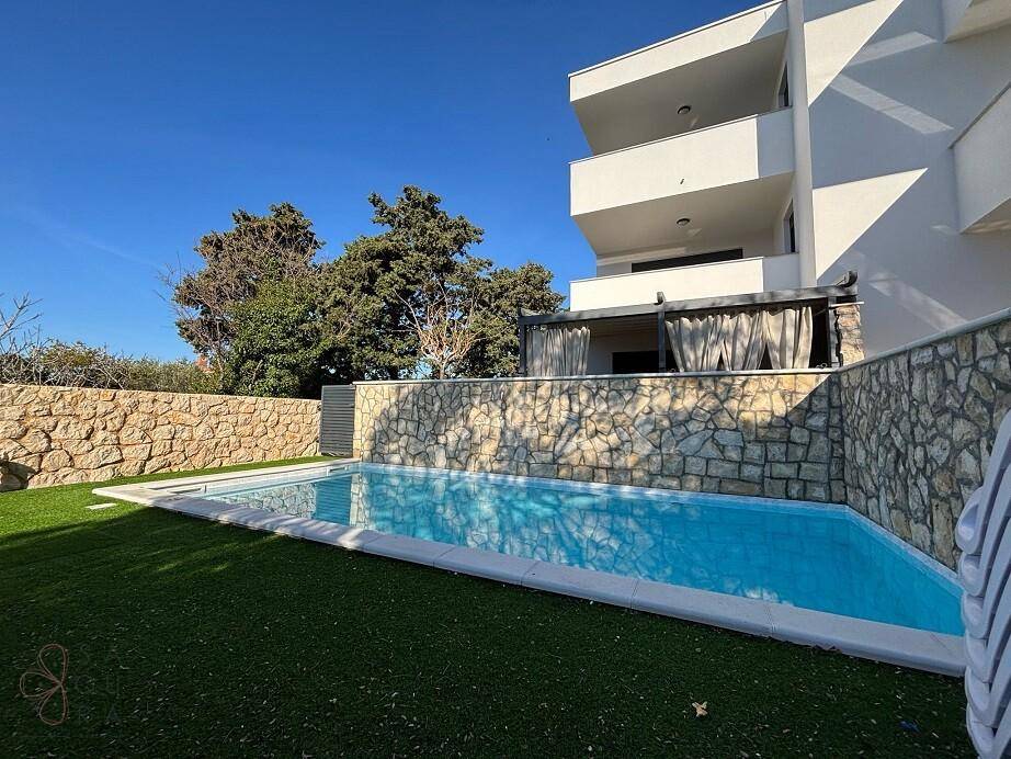 Seitliche Ansicht des modernen Gebäudes mit Poolbereich und Steinmauer im Sonnenschein.