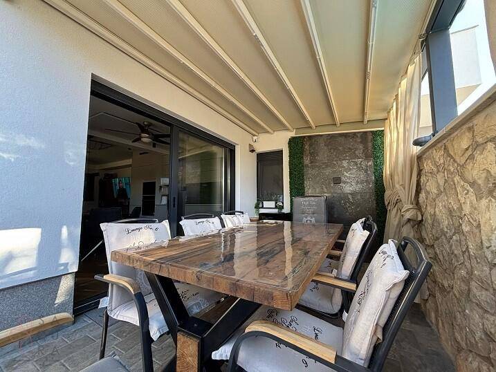 Überdachte Terrasse mit modernem Esstisch und Stühlen, ideal für Mahlzeiten im Freien.