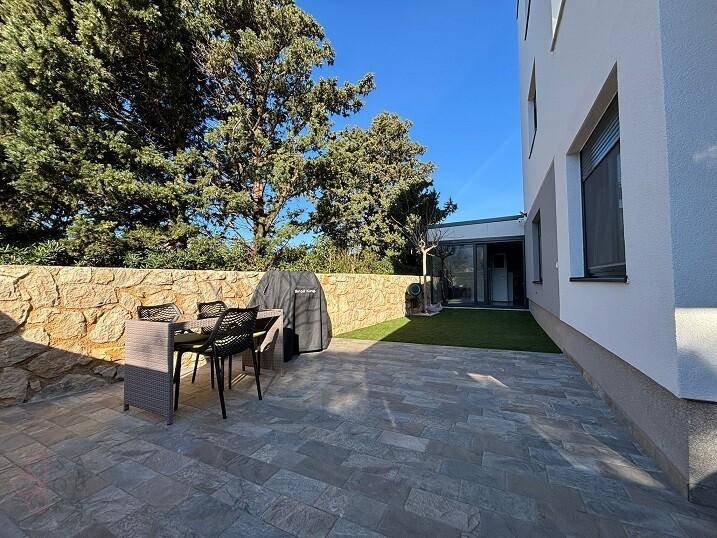 Gepflasterte Terrasse mit Grillbereich und Gartenmöbeln neben dem Gebäude.