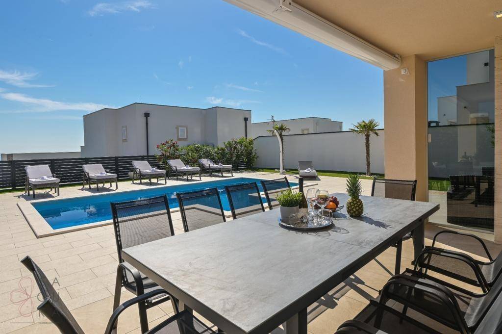 Geräumige Terrasse mit Esstisch und Poolblick, ideal für Mahlzeiten im Freien unter der Sonne.