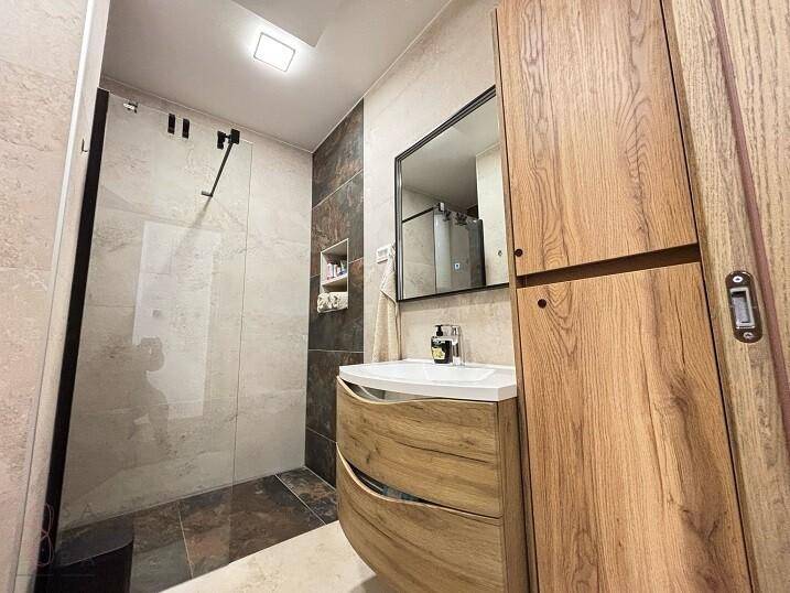 Modernes Badezimmer mit begehbarer Dusche, Holzwaschtisch und eleganten Fliesen.