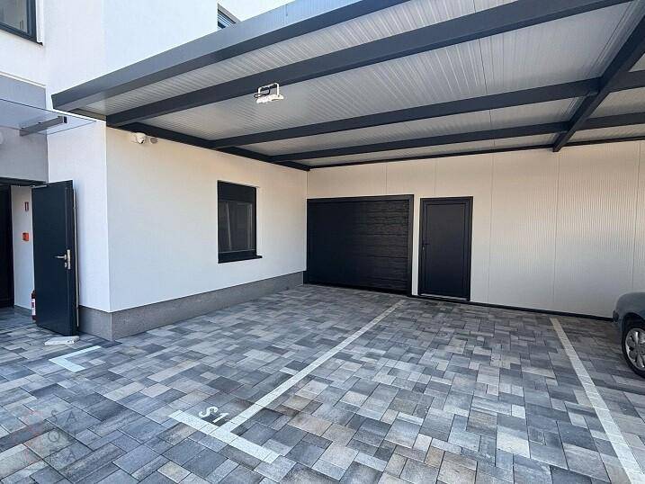 Überdachter Parkplatz mit Pflastersteinen und Garagentoren für mehrere Fahrzeuge.