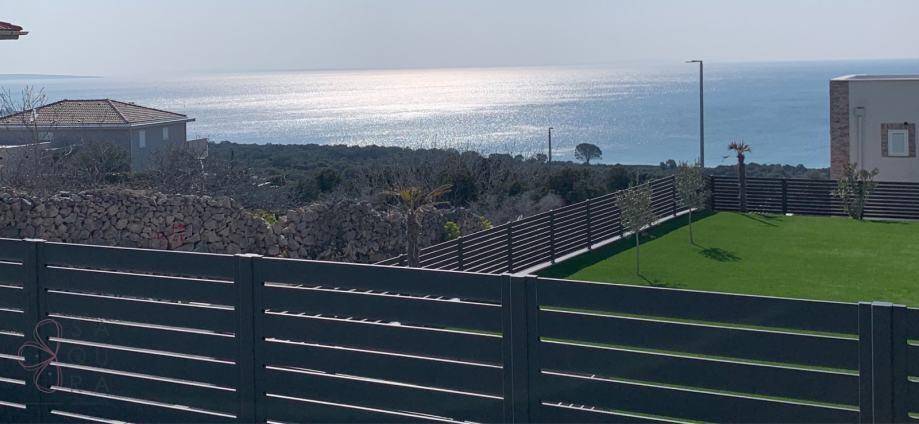 Weitläufiger Meerblick über einen gepflegten Garten und modernen Zaun.