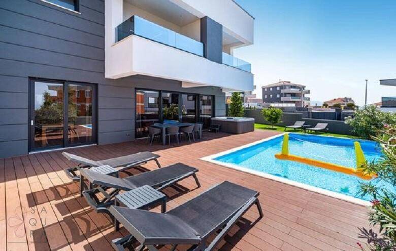Geräumige Holzterrasse mit Sonnenliegen und Blick auf den Pool und die moderne Villa.