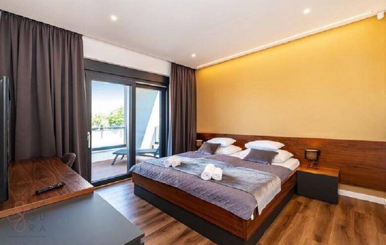 Gemütliches Schlafzimmer mit Holzbett, gelber Akzentwand und Zugang zu einem sonnigen Balkon.