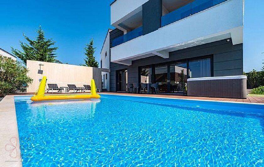 Großzügiger Poolbereich mit Holzdeck und aufblasbarem Spielzeug vor der modernen Villa.