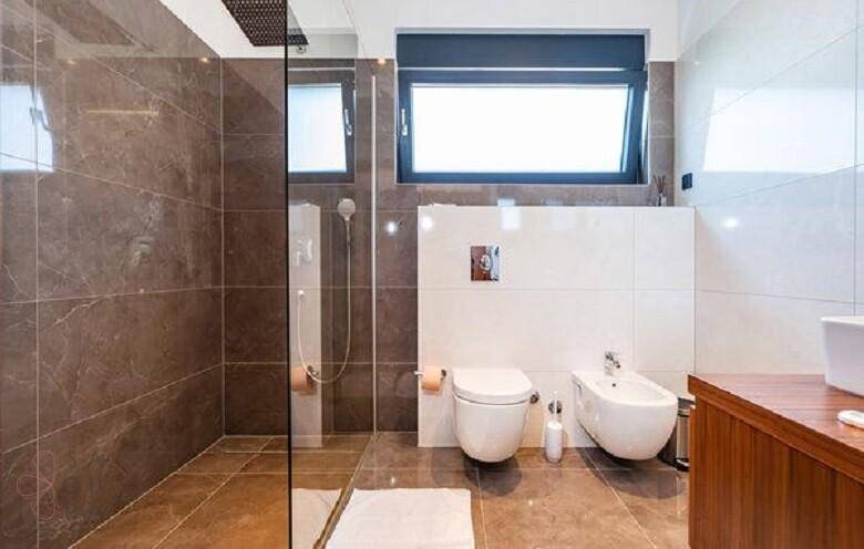 Modernes Badezimmer mit großer begehbarer Dusche, Toilette, Bidet und Fenster.