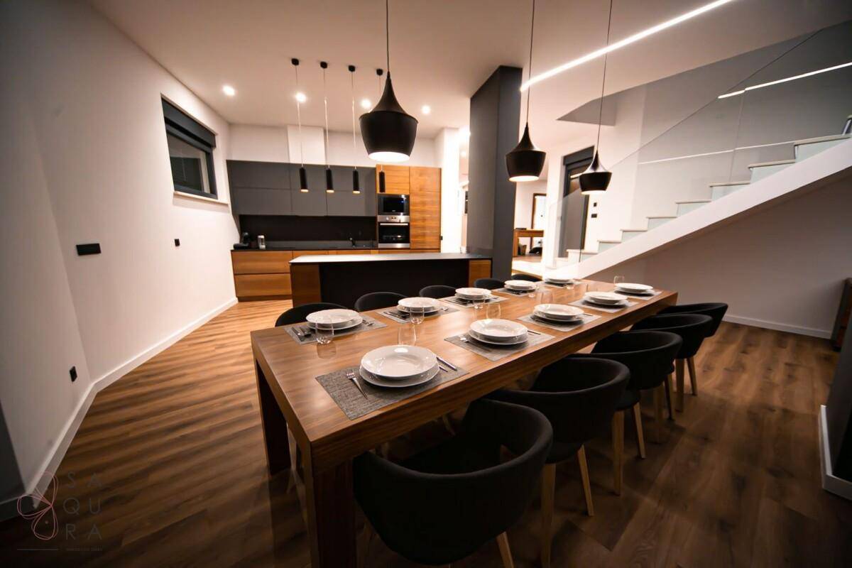 Eleganter Essbereich mit großem Holztisch und moderner Küche im Hintergrund, ideal für gesellige Abende.