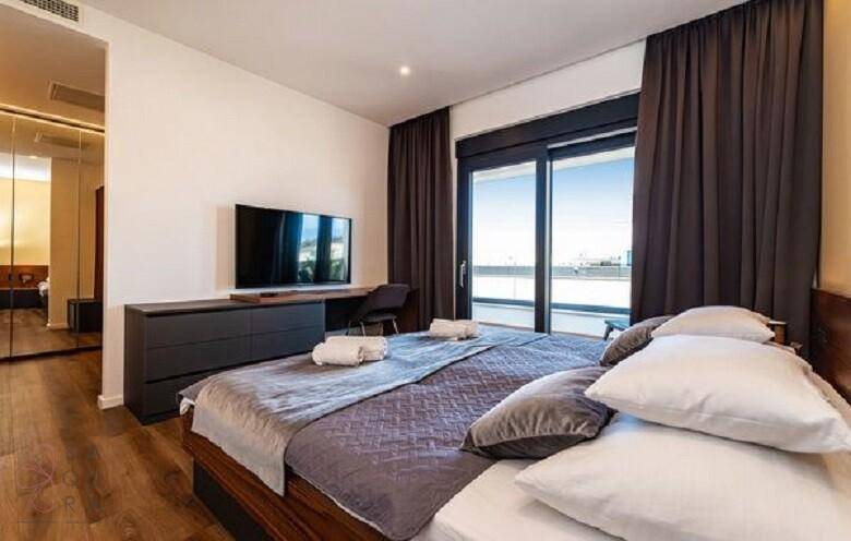 Modernes Schlafzimmer mit großem Bett, Fernseher und Schiebetüren zum Außenbereich.