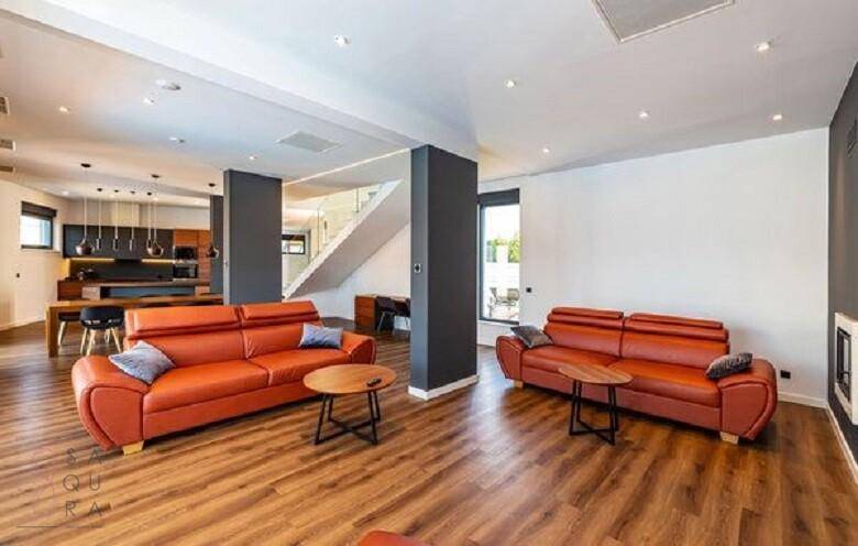 Helles, offenes Wohnzimmer mit modernen orangefarbenen Sofas und Holzboden, verbunden mit Essbereich.