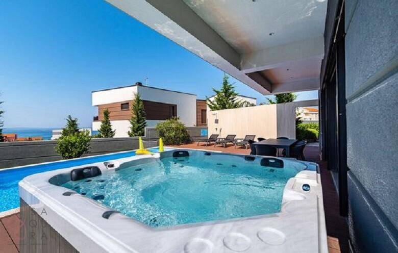 Entspannender Whirlpool auf der Holzterrasse mit Meerblick und angrenzendem Poolbereich.
