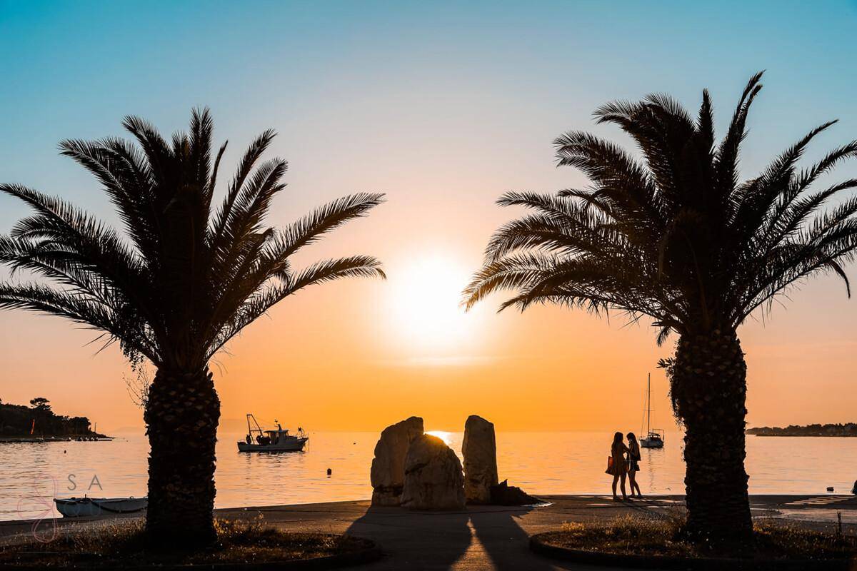 Atemberaubender Sonnenuntergang über dem Meer mit Palmen und Menschen am Ufer.