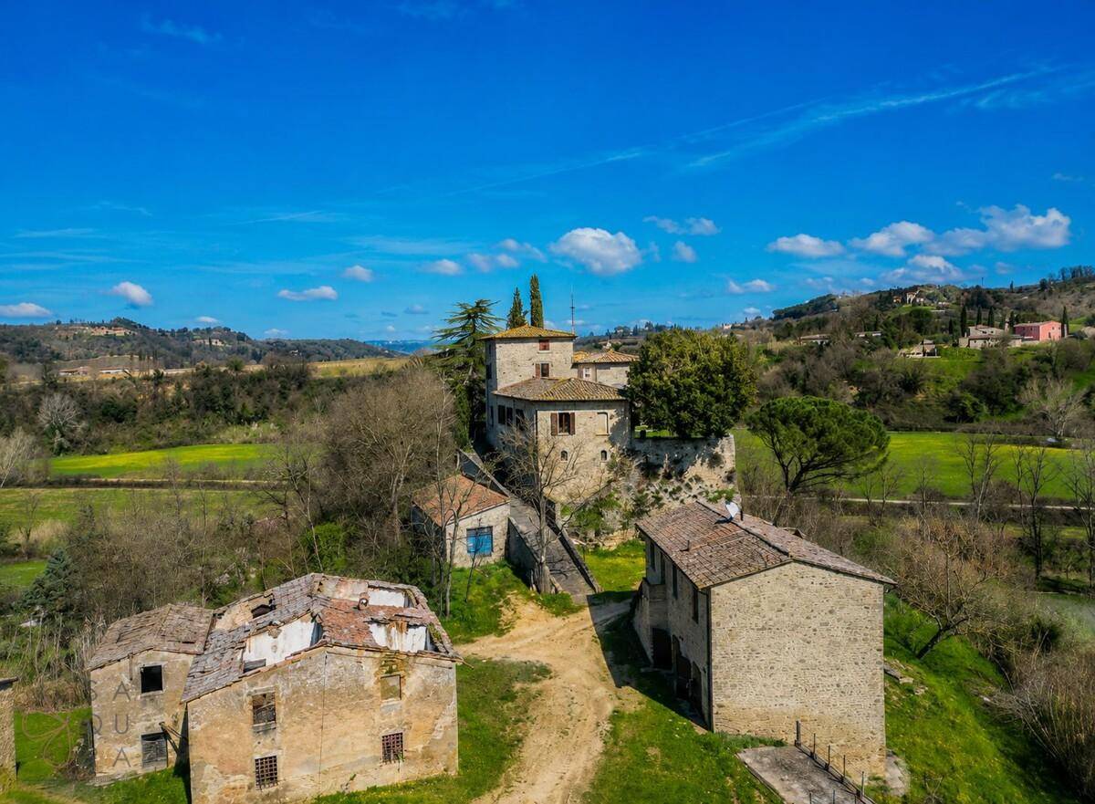 Luftaufnahme eines historischen Anwesens mit mehreren Steingebäuden, teils renovierungsbedürftig, in grüner Landschaft.