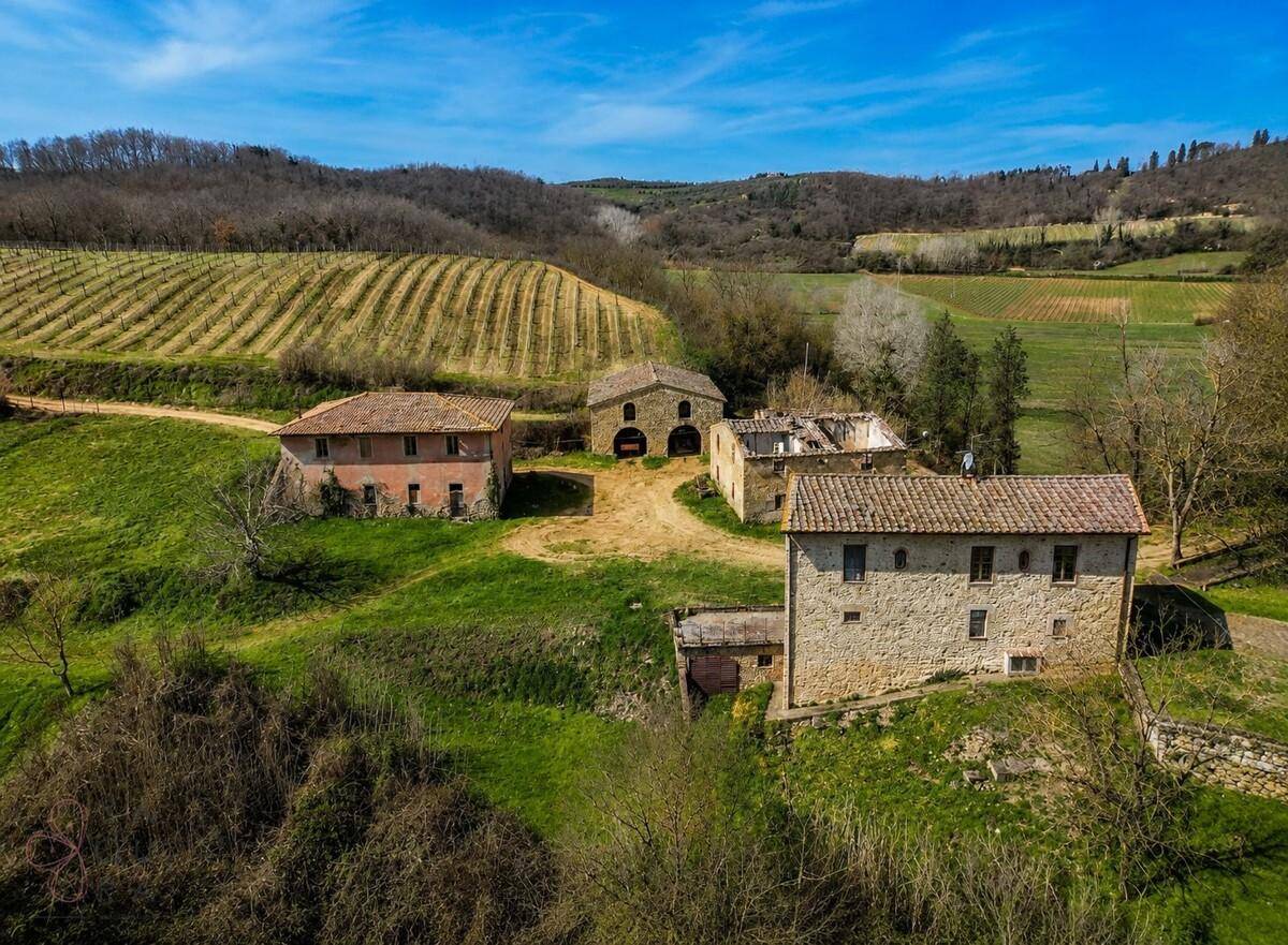 Luftaufnahme eines Anwesens mit mehreren historischen Gebäuden, umgeben von Weinbergen und grünen Wiesen.