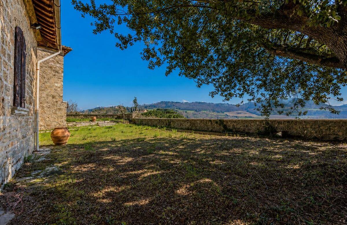 Großer Gartenbereich neben einem Steinhaus mit niedriger Steinmauer und weitem Landschaftsblick.