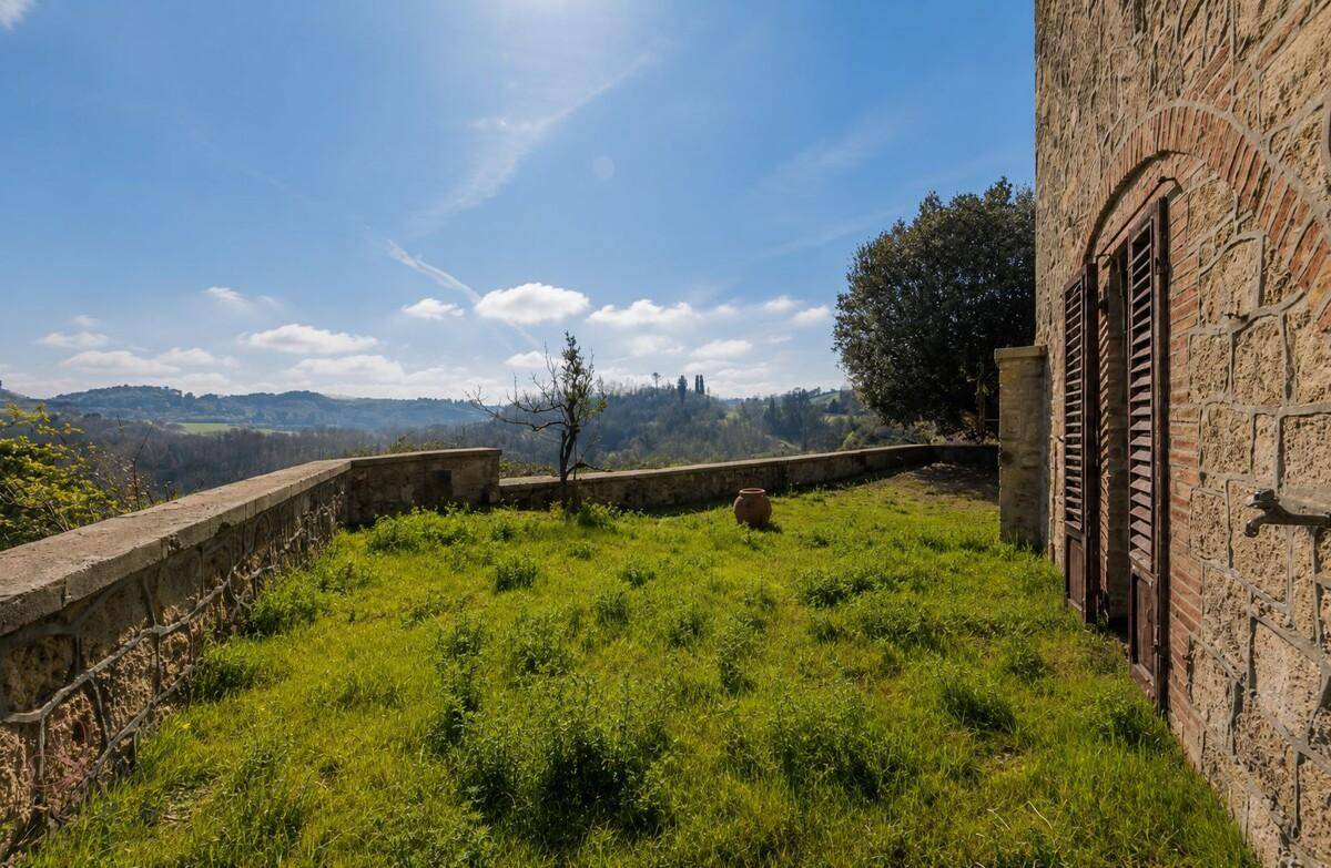 Sonniger Gartenbereich mit frischem Grün, umgeben von einer Steinmauer und weitem Ausblick.