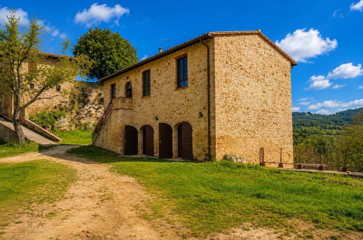 Rustikales Steinhaus mit mehreren Holztüren und einem Balkon, umgeben von grüner Natur.