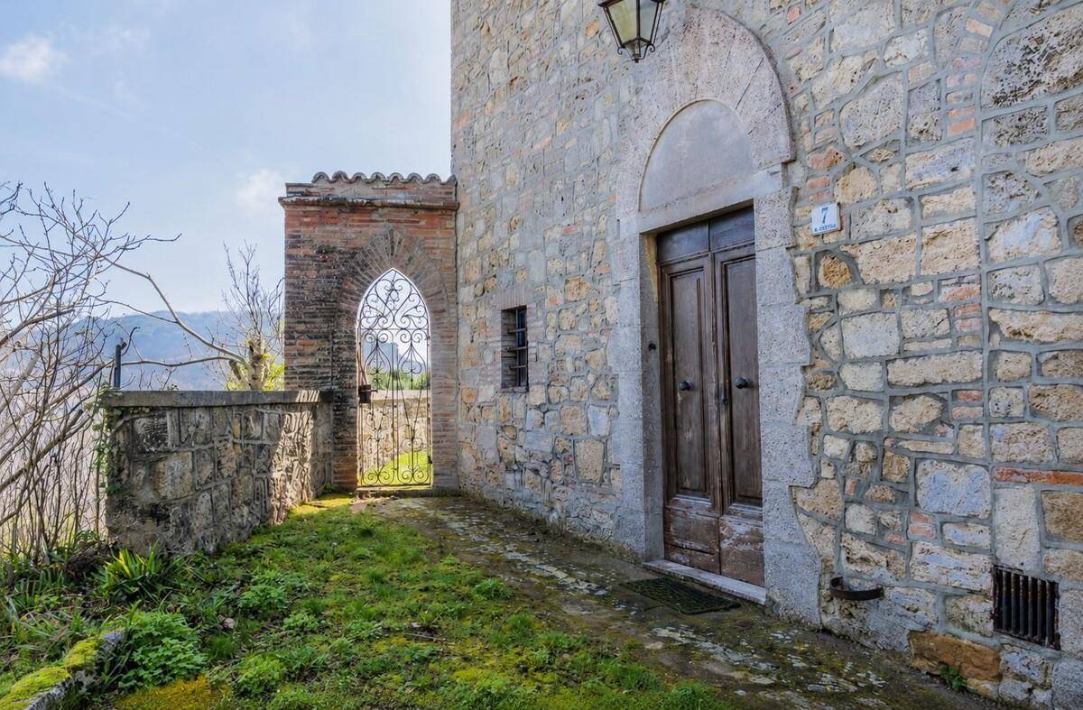 Historischer Eingangsbereich eines Steinhauses mit schmiedeeisernem Tor und Blick auf die Landschaft.