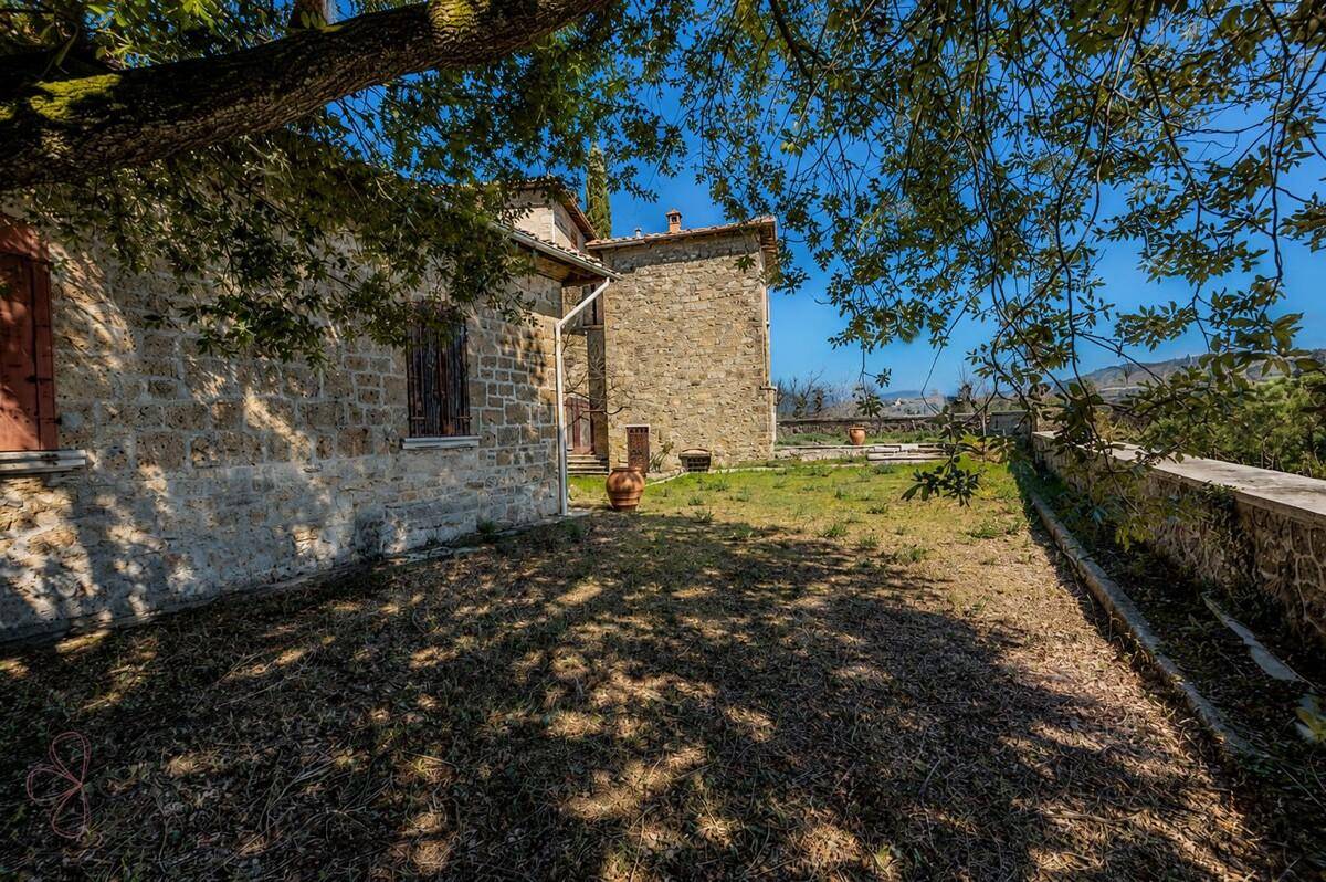 Schattiger Gartenbereich neben einem historischen Steinhaus mit Blick auf die umliegende Natur.