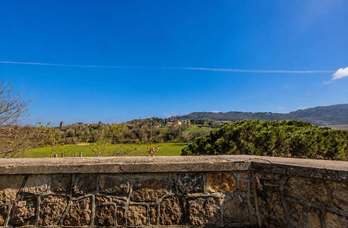 Steinmauer mit weitem Blick über die grüne Hügellandschaft unter blauem Himmel.