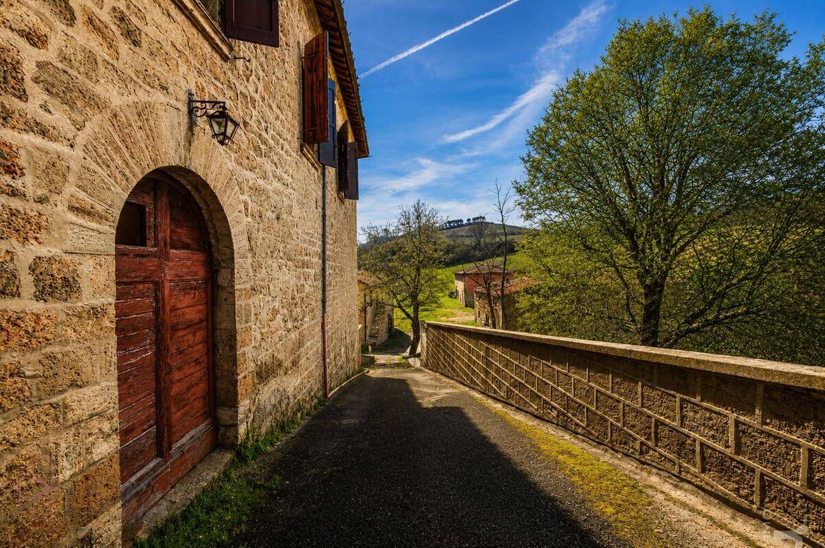 Schmaler Weg entlang eines historischen Steinhauses mit Blick auf die umliegende Landschaft.