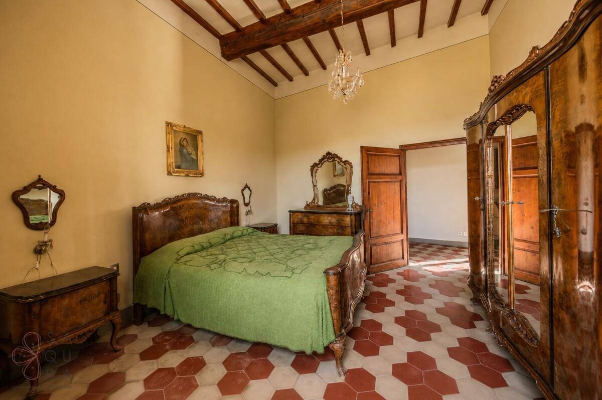 Elegantes Schlafzimmer mit antiken Holzmöbeln, Holzbalkendecke und traditionellem Fliesenboden.