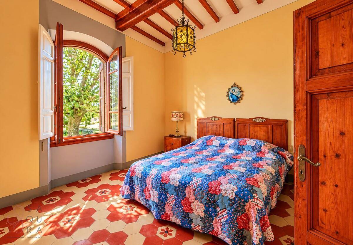 Gemütliches Schlafzimmer mit Holzbalkendecke, farbenfroher Bettdecke und Blick auf die Landschaft.