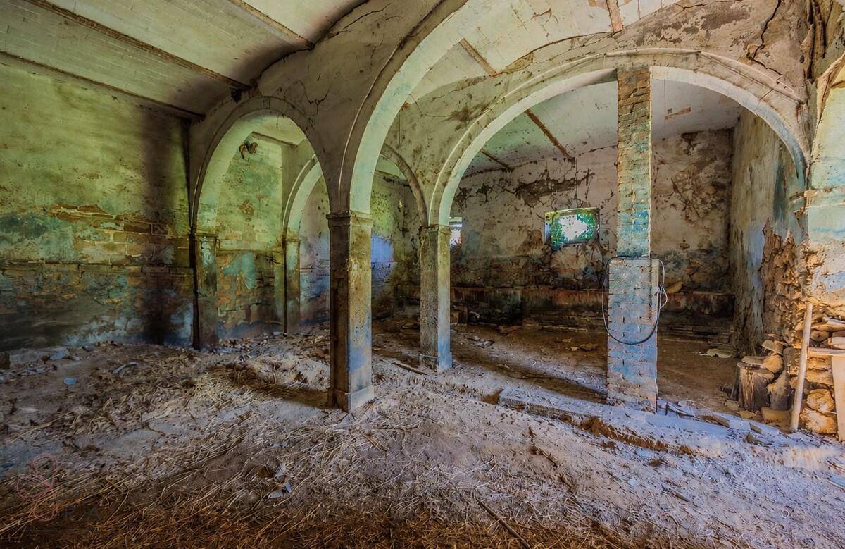 Geräumiger Kellerraum mit mehreren Bögen, Säulen und Spuren alter Wandfarben.