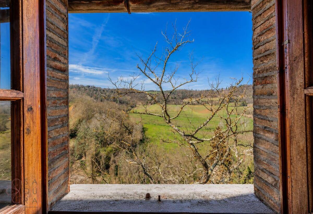 Weitläufiger Blick aus dem Fenster auf die hügelige, grüne Landschaft unter blauem Himmel.