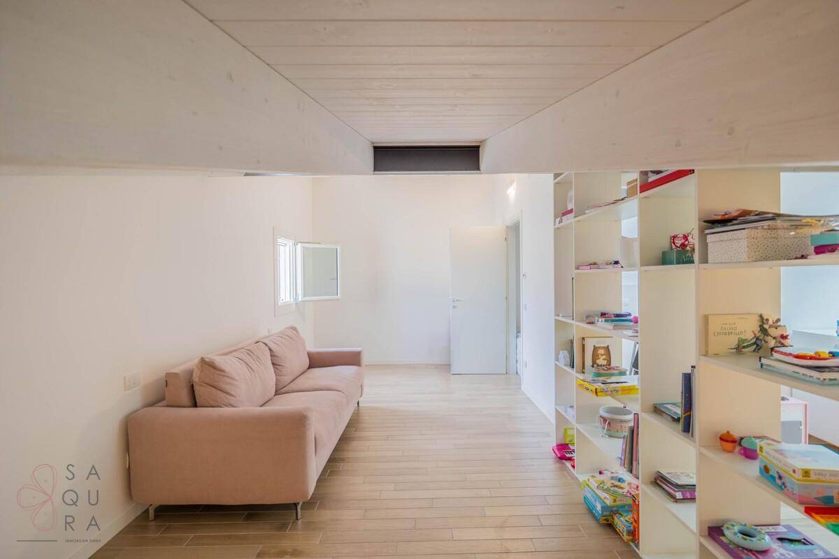 Heller Dachbodenbereich mit Schrägen, Bücherregalen und einem bequemen Sofa.